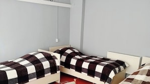A room with three single beds, a table with a patterned tablecloth, and a hanging light fixture. - Sabir iki (Baku)