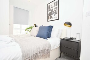 A bedroom with a bed, bedside table, lamp, and a framed artwork on the wall.