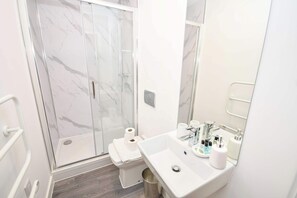 A modern bathroom with a glass shower enclosure, a white sink with toiletries, and a large mirror.