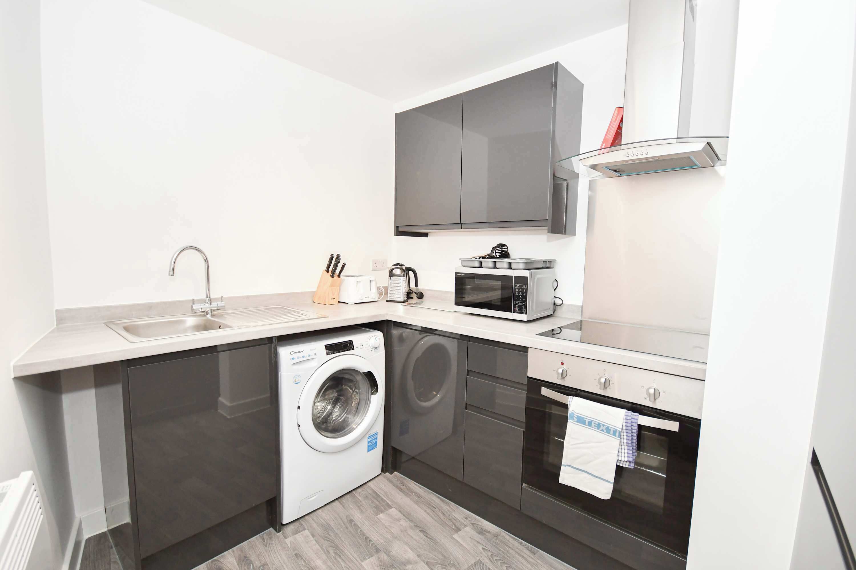 A compact kitchen with a washing machine, microwave, oven, and a sink.