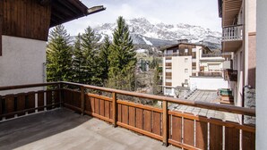 A balcony with a wooden railing overlooking a mountainous landscape with snow-covered peaks.