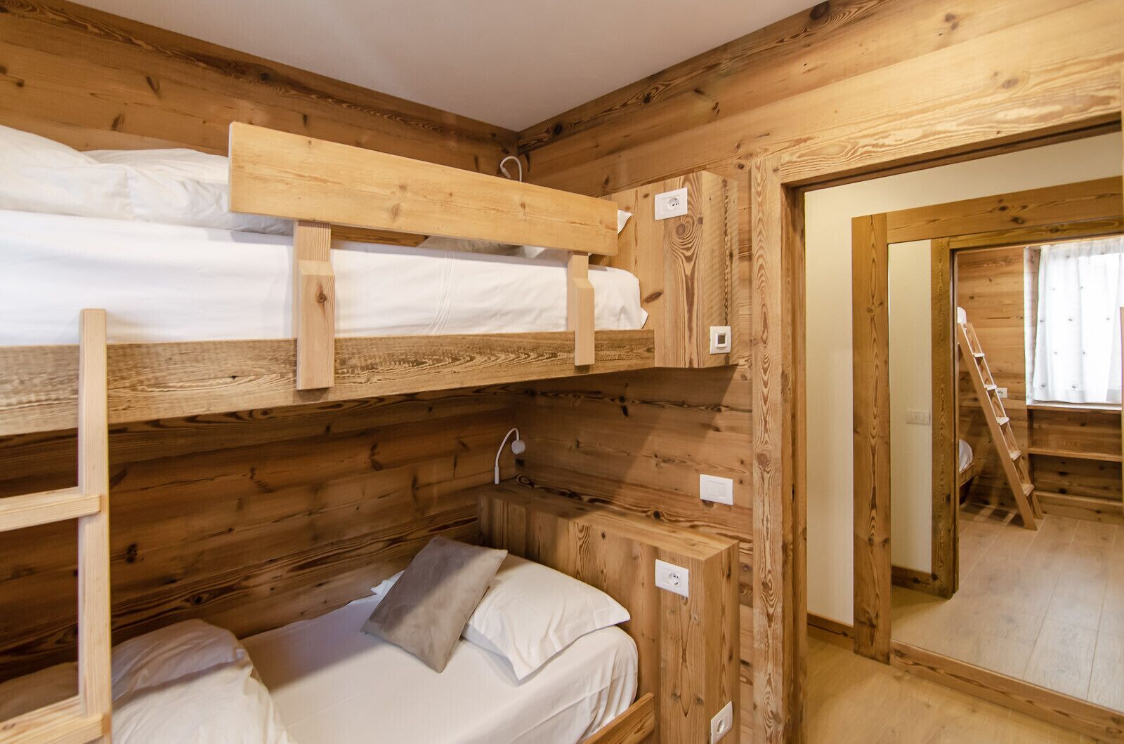 A wooden cabin-style room with bunk beds, a small bathroom, and a wooden ladder.
