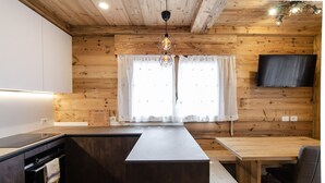 A modern kitchen with wooden walls, a central island, a dining table, and a flat-screen TV mounted on the wall.