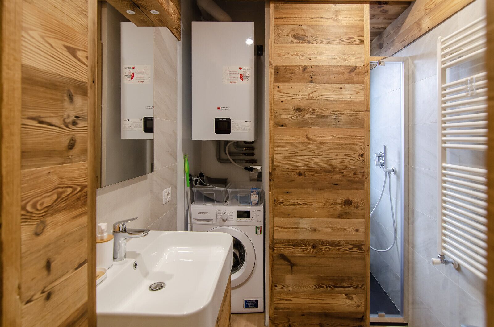 A compact bathroom with a sink, washing machine, and shower.
