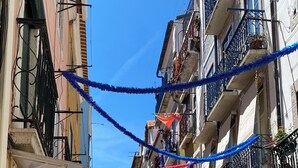 A narrow cobblestone street lined with multi-story buildings, some with balconies and outdoor decorations. - Portuguese Classic Flat at Lisbon Historic Center (Lisboa)
