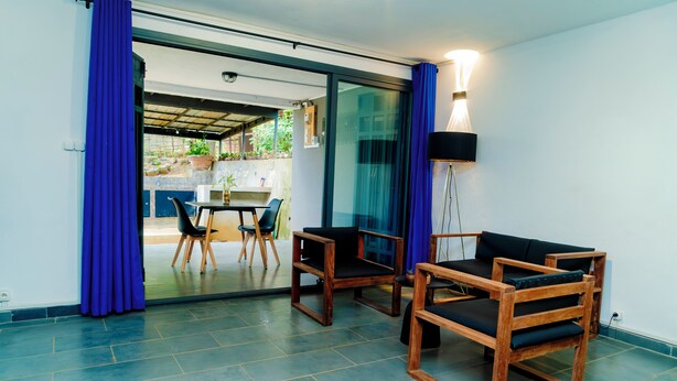 A modern room with a glass door leading to a balcony, a dining area with a table and chairs, and a black floor lamp. - Cattleya Guest House (Nosy Be)