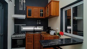 A compact kitchen with wooden cabinets, a gas stove, a sink, and a window. - Cattleya Guest House (Nosy Be)