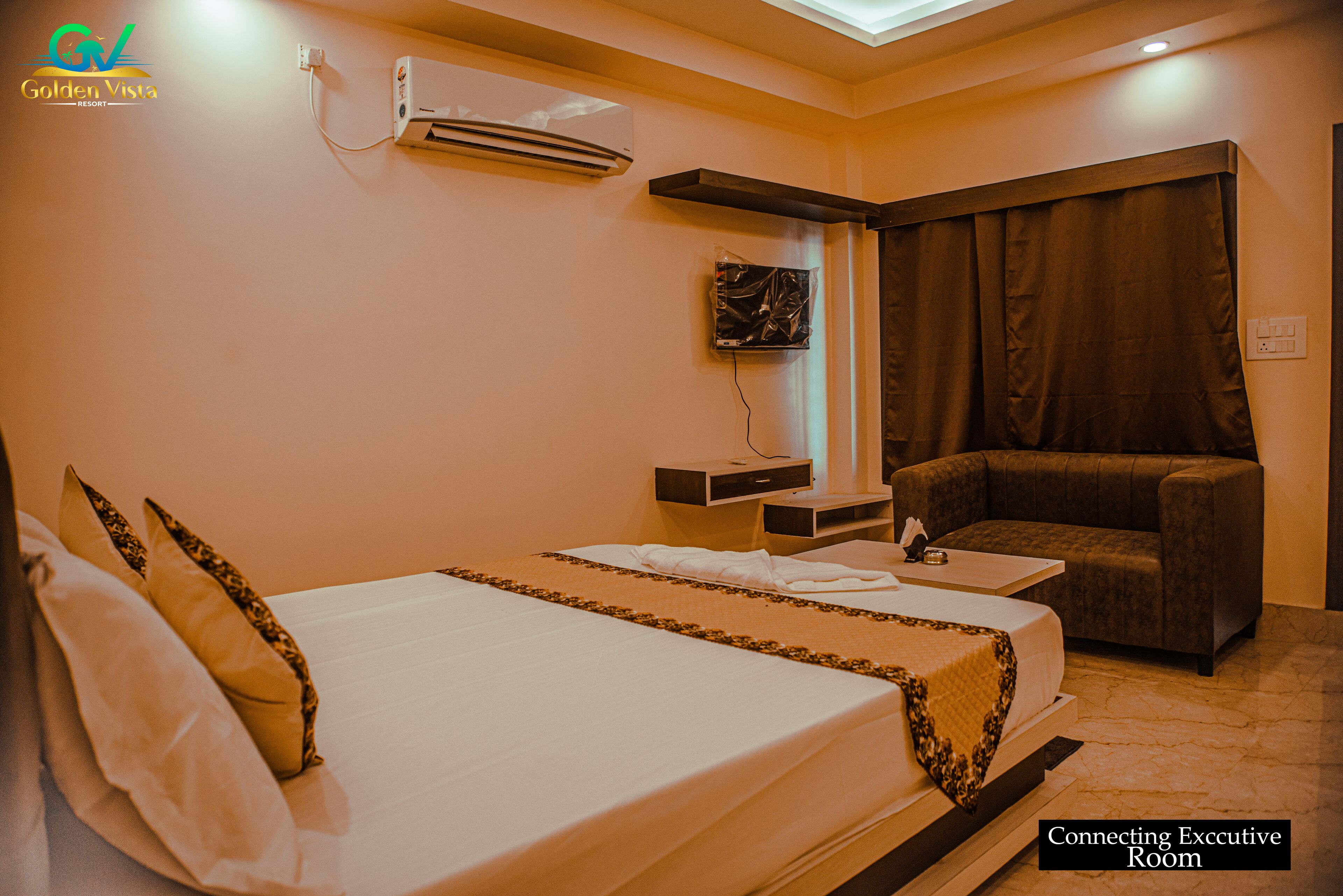 A hotel room with a bed, a desk, a chair, and a wall-mounted air conditioner.
