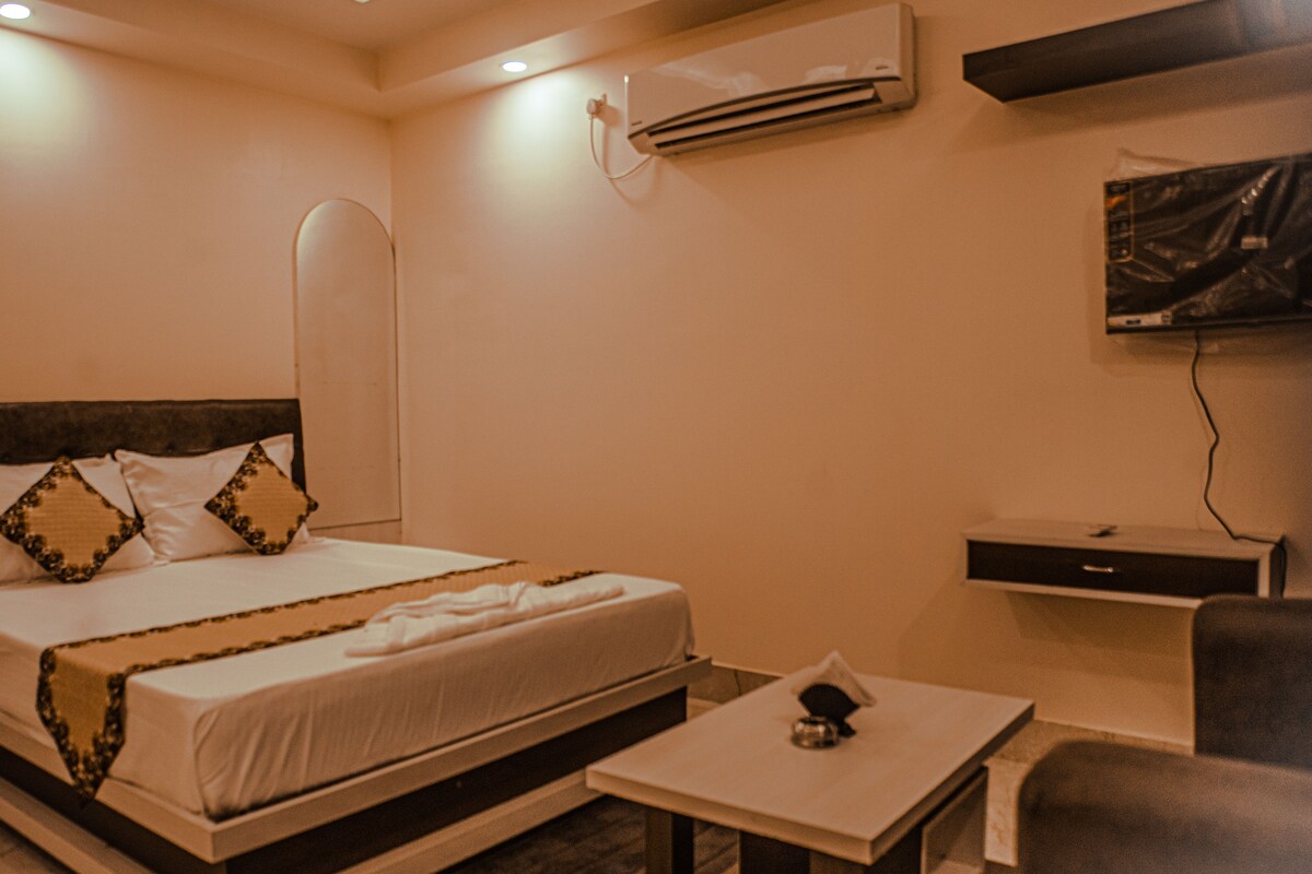 Een hotelkamer met een bed, nachtkastje, airconditioning en een aan de muur bevestigde televisie.