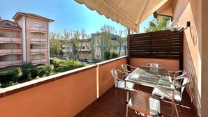 A balcony with a glass table and chairs, a beige awning, and a view of neighboring buildings. - Veliero Flexrent - Abyssinia Real Estate (Riccione)