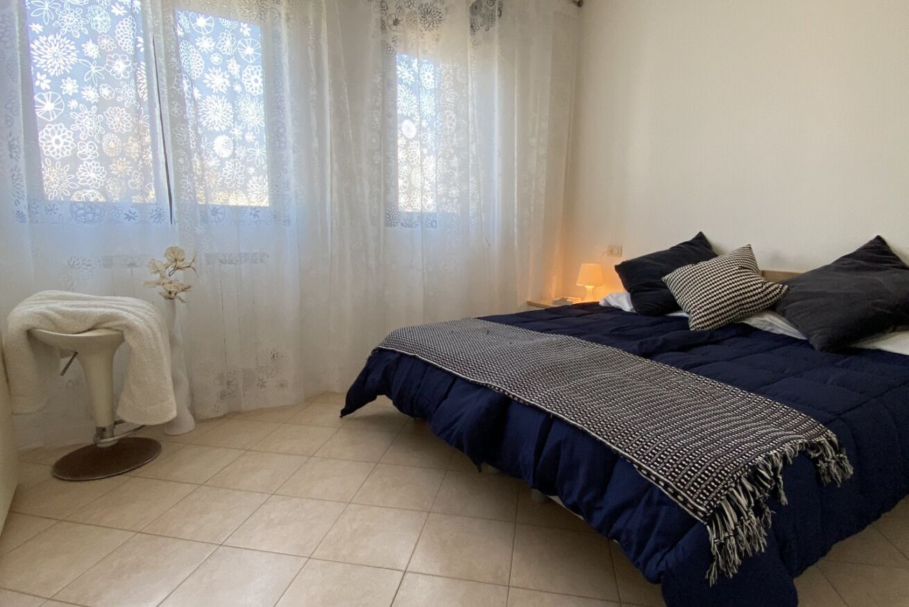 Um quarto com uma cama, uma cadeira e uma janela com cortinas.