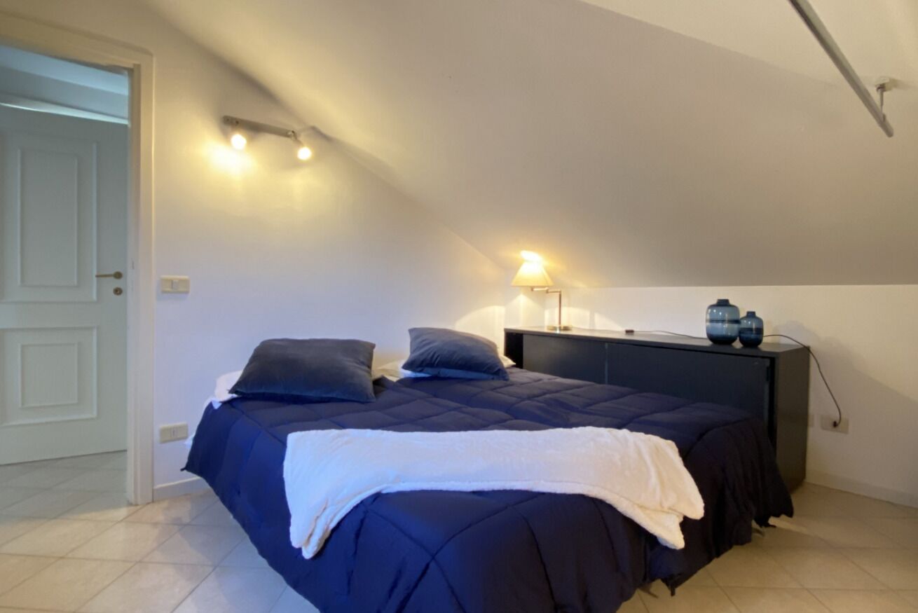 Un dormitorio con cama, mesita de noche, lámpara y dos jarrones.