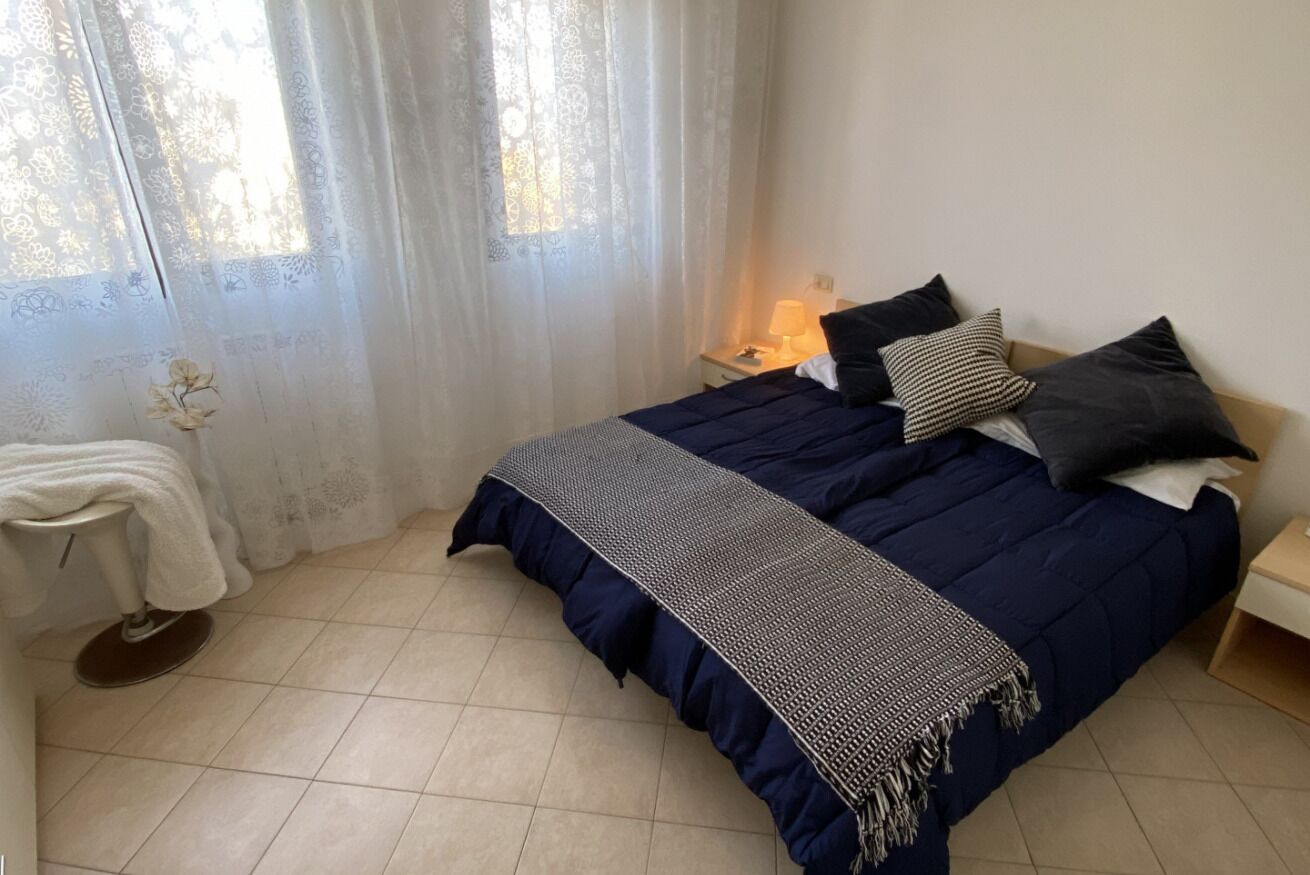 A bedroom with a bed, a nightstand, a lamp, and a window with curtains.