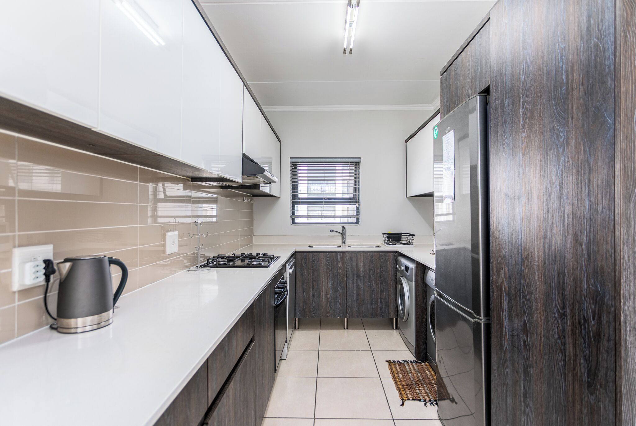 A modern kitchen with white cabinets, a stainless steel kettle, a gas stove, a built-in oven, and a refrigerator.