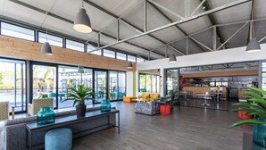 Un vaste espace intérieur doté d’un haut plafond, de grandes fenêtres et d’un agencement varié comprenant des canapés et des tables.