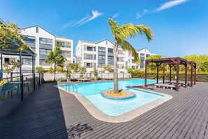 A pool area with a wooden deck, lounge chairs, a palm tree, and a gazebo. - The Sandown 178 by CTHA (Cape Town)