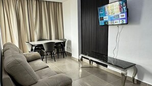 Una sala de estar moderna con un sofá, una mesa de comedor con sillas y un televisor de pantalla plana montado en la pared.