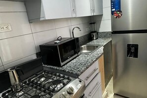 Eine kompakte Küche mit Gasherd, Mikrowelle, Spüle und einem Edelstahl-Kühlschrank.