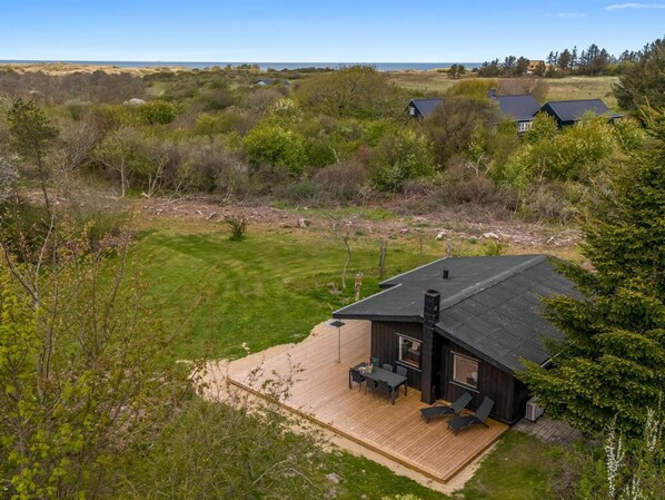 A cabin with a deck, surrounded by natural landscape and a view of the sea.