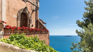 Um edifício costeiro com porta de madeira, flores vermelhas e vista para o mar.