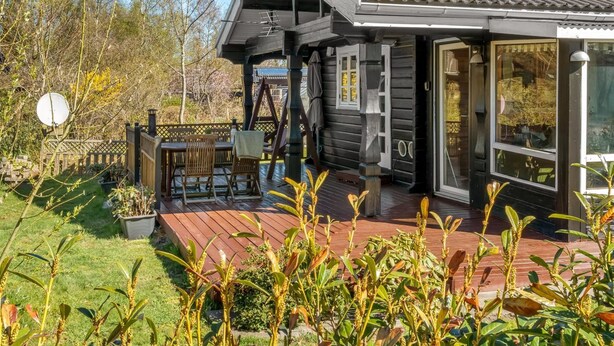 Een houten huis met een terras, een overdekte veranda en een groot raam.