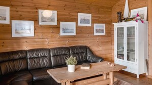 Een gezellig ingerichte blokhut met een leren bank, een houten salontafel en een kast met glazen deuren.