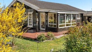 Een houten huis met een veranda, grote ramen en een omheinde tuin.