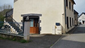 Un edificio de dos pisos con fachada color beige, una puerta de madera y una ventana pequeña.