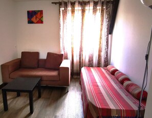 Un salon avec un canapé, une table, un lit avec une literie à rayures, une lampe et un tableau accroché au mur.