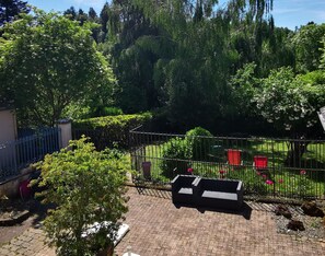 Un jardin avec une zone dallée, une clÎture en métal et un banc.