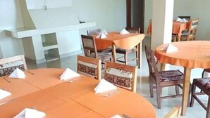 Comedor con mesas redondas cubiertas con manteles naranjas, cada una con un servilleta blanca y cubiertos.