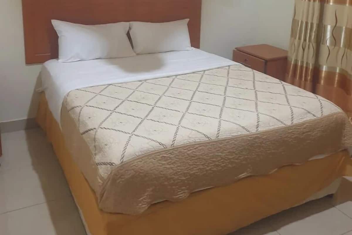A standard hotel room with a single bed, a nightstand, a wall-mounted lamp, and a curtain.