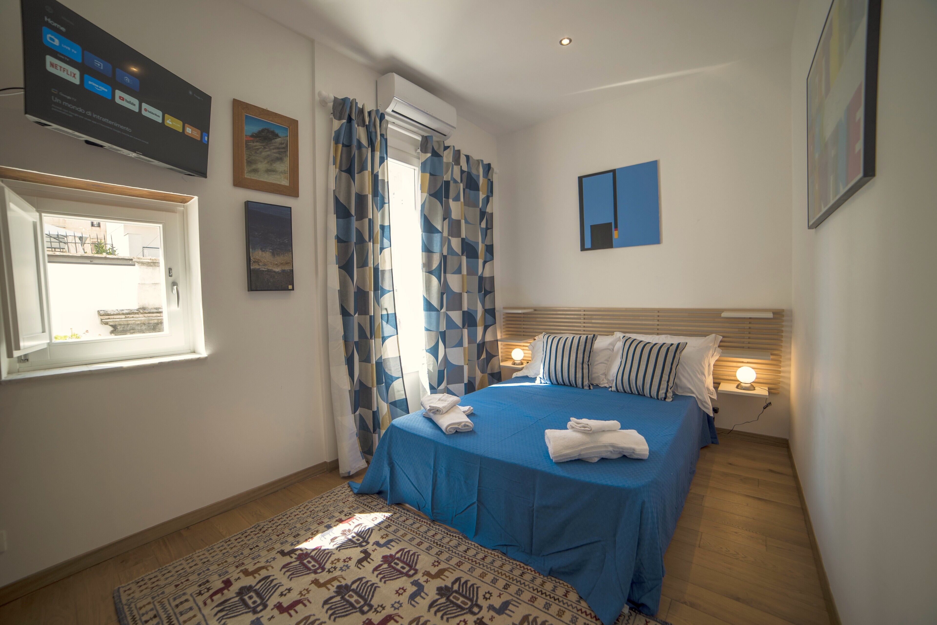 A bedroom with a bed, a TV mounted on the wall, a window, and a door.