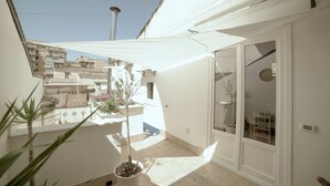 Een balkon met plantenbakken, een witte luifel en uitzicht op omliggende gebouwen.