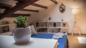 Een potplant op een tafel in een kamer met een blauw bed, houten balken en een boekenkast.