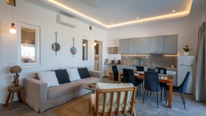 A modern living room with a sofa, dining table, chairs, and a kitchen area with cabinets and appliances. - Premium 2 Bedroom House with Private Pool (Mykonos)