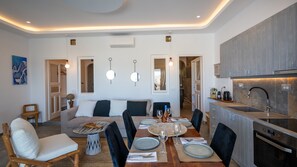 A modern kitchen with a built-in oven, a dining area with a round table and chairs, and a living room with a sofa and a coffee table.