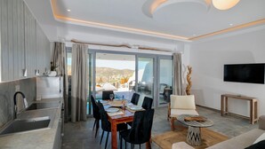 A modern living room with a dining area, a kitchen, and a large sliding glass door leading to an outdoor terrace. - Premium 2 Bedroom House with Private Pool (Mykonos)