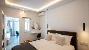 A modern hotel room with a large bed, a bedside table, a mirror, and a view of the hallway. - Premium 2 Bedroom House with Private Pool (Mykonos)