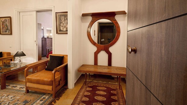 Een kamer met een houten stoel, een klein tafeltje, een spiegel en een kledingkast.