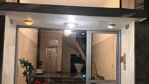 Een moderne gevel met een glazen deur, een trap naar een hoger niveau en potplanten op de begane grond.
