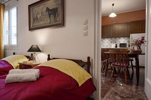Une chambre avec deux lits, un tableau, une lampe et une vue sur un coin cuisine avec des meubles en bois et une table à manger.