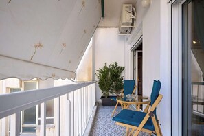Un balcón con toldo blanco, una planta en maceta y dos sillas azules.