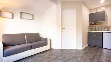A modern kitchen with dark wooden flooring, a grey sofa, and a white door.