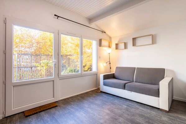 Une pièce avec un canapé blanc, un lampadaire et une vue dégagée sur l’extérieur grâce à de grandes fenêtres.