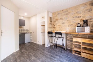 Une cuisine compacte avec un mur en pierre, un four à micro-ondes et deux tabourets de bar.