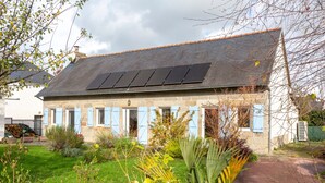 A stone building with a sloped roof, solar panels, and blue shutters.