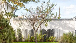 A garden with a tree, a wooden fence, and a white wall.
