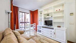 A living room with a sofa, TV stand, and a dining area with a table and chairs.