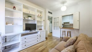 A modern living room with a TV, white entertainment unit, wooden flooring, and a beige sofa.